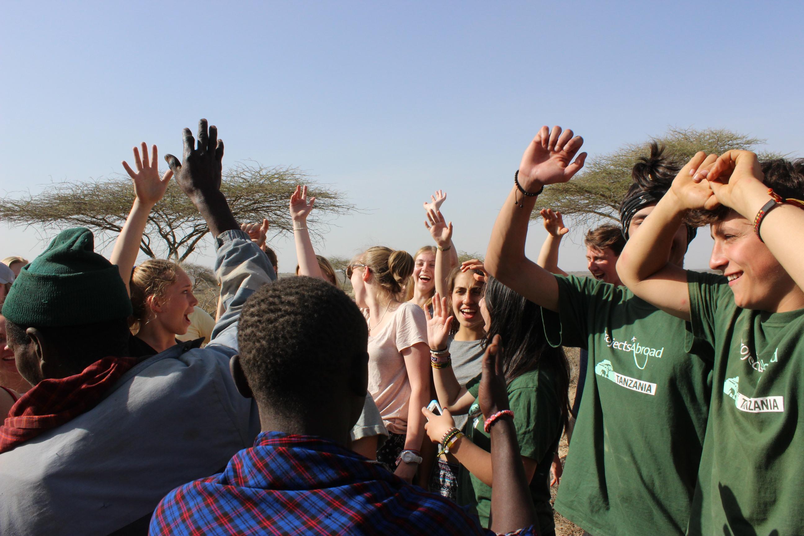 Group of Projects Abroad Community Staff holding their hands up at a group visit to the Maasai Community during Cultural Immersion in Tanzania. Group of Culture and Community staff enjoy a group activity at a day visit to the Maasai Community during their Community Volunteer Work in Tanzania.